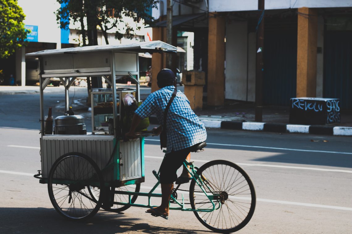 Vendedor de comida pedalando a bicicleta que foi improvisada para levar os seus produtos.