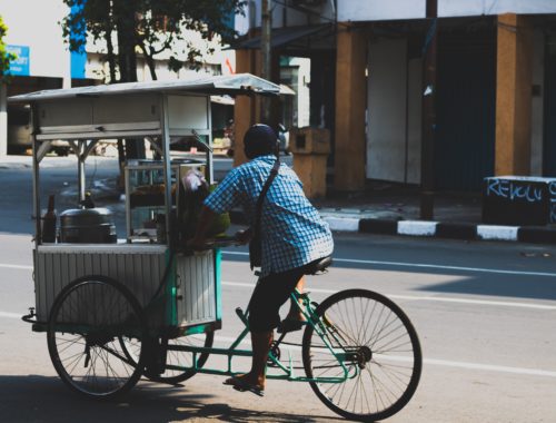 Vendedor de comida pedalando a bicicleta que foi improvisada para levar os seus produtos.