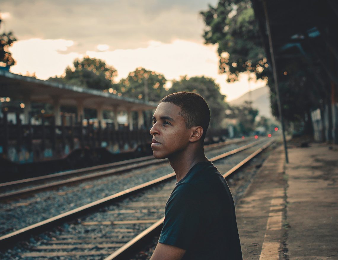 Jovem negro sentado na linha de trem refletindo sobre o racismo no Brasil