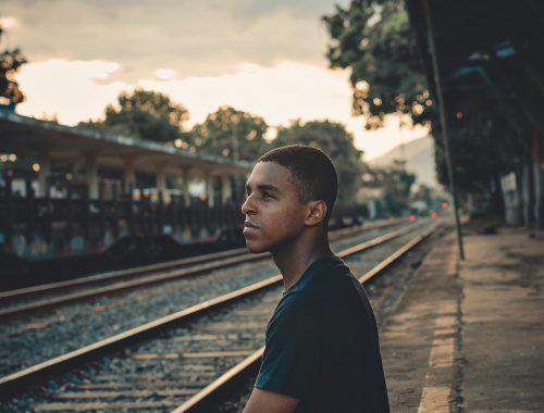 Jovem negro sentado na linha de trem refletindo sobre o racismo no Brasil